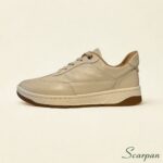 Foto de estúdio de um Tênis Feminino de Couro com Elástico, na cor predominantemente branca, com detalhes em preto (ou cor escura, dependendo da visualização do detalhe na parte superior/calcanhar) e solado de borracha. O elástico no peito do pé facilita o calce, destacando a praticidade do design.