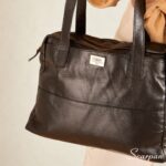 Bolsa de couro legítimo preta com três divisórias modelo Cibeli Scarpan vista em detalhe de fente com alças de ombro.