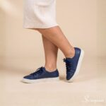 Tênis Feminino de Couro Marinho Mia da Scarpan em foto lateral/de perfil nos pés, combinado com saia midi off-white. Tênis casual em couro legítimo azul-marinho com solado reto off White e cadarços marinho.