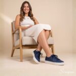 Modelo feminina sentada usando o Tênis Feminino de Couro Marinho Mia da Scarpan com vestido de tricô canelado off-white. Look casual elegante com tênis de couro marinho e solado Off White.