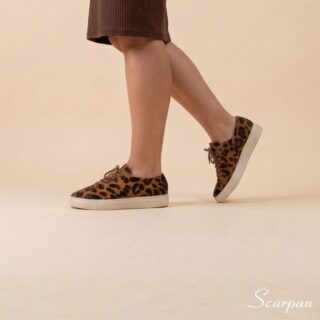 Tênis Feminino de Couro Pelo Onça Mia da Scarpan em ângulo de perfil em movimento. Modelo com estampa animal print de onça, cadarço marrom e solado Off White em TR, combinado com vestido marrom.