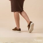 Visão traseira e lateral do Tênis Feminino de Couro Pelo Onça Mia da Scarpan em movimento. Destaque para o acabamento em couro com pelo estampado, cadarço marrom e a base do solado antiderrapante Off White em TR.
